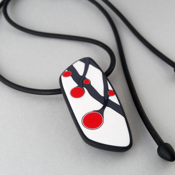 Handmade necklace with a single bead showing a graphic flower bud motif in red, on a white background with a charcoal border. It is approximately 2.6 cm wide and 6.4 cm long and hangs on a black adjustable cord.