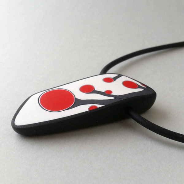 Handmade necklace with a single bead showing a graphic flower bud motif in red, on a white background with a charcoal border. It is approximately 2.6 cm wide and 6.4 cm long and hangs on a black adjustable cord.