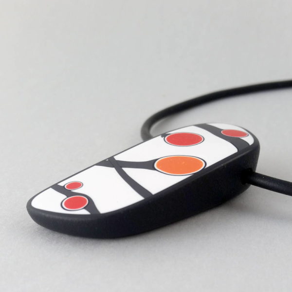 Handmade pendant showing a graphic flower bud motif in orange tones, on a white background with a charcoal border. It is approximately 2.6 cm wide and 6.4 cm long and hangs on a black adjustable cord.