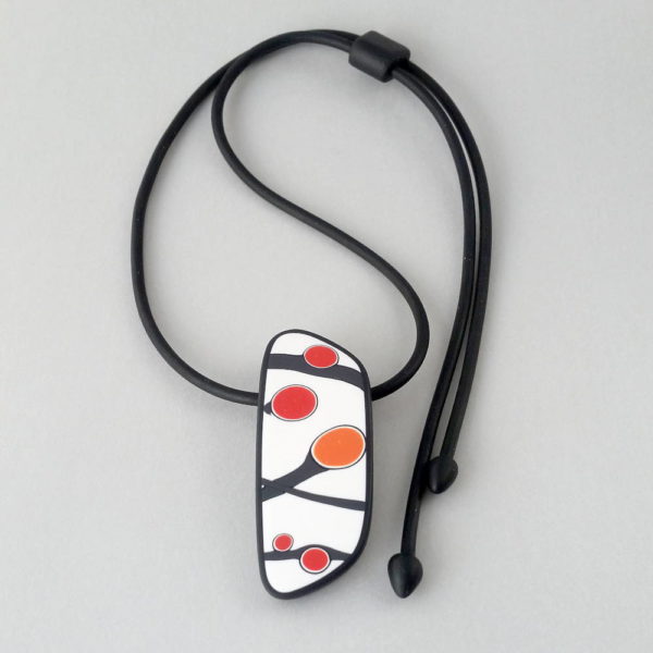 Handmade pendant showing a graphic flower bud motif in orange tones, on a white background with a charcoal border. It is approximately 2.6 cm wide and 6.4 cm long and hangs on a black adjustable cord.