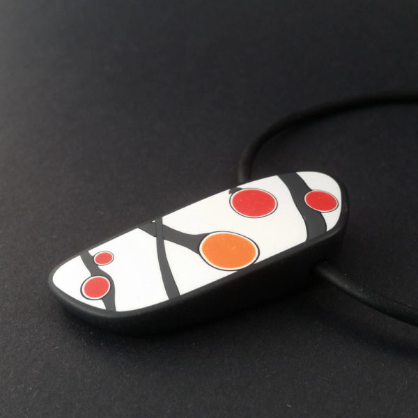 Handmade pendant showing a graphic flower bud motif in orange tones, on a white background with a charcoal border. It is approximately 2.6 cm wide and 6.4 cm long and hangs on a black adjustable cord.