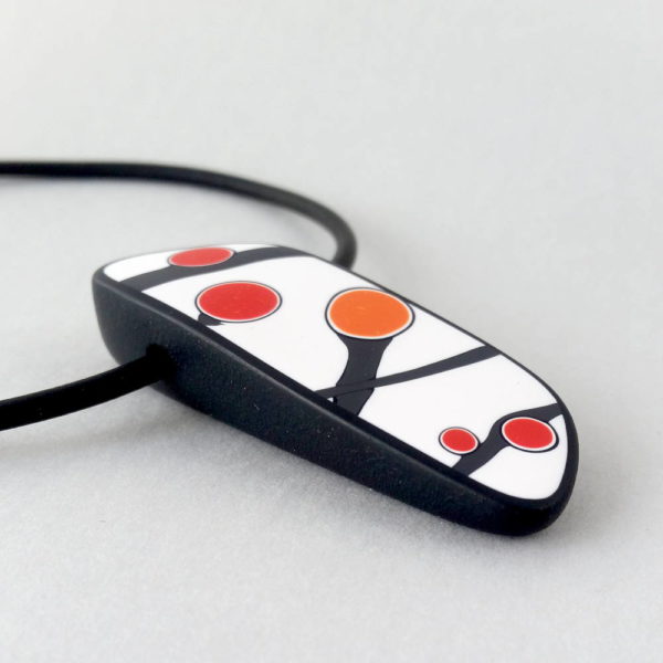 Handmade pendant showing a graphic flower bud motif in orange tones, on a white background with a charcoal border. It is approximately 2.6 cm wide and 6.4 cm long and hangs on a black adjustable cord.