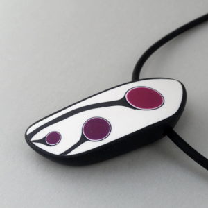 Handmade shield shaped necklace featuring an abstract flower bud motif in plum on a white background, with charcoal border. It is approximately 2.6 cm wide and 6. long and hangs on a black adjustable cord.