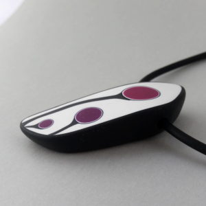 Handmade shield shaped necklace featuring an abstract flower bud motif in plum on a white background, with charcoal border. It is approximately 2.6 cm wide and 6. long and hangs on a black adjustable cord.