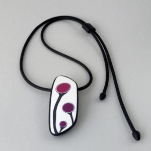 Handmade shield shaped necklace featuring an abstract flower bud motif in plum on a white background, with charcoal border. It is approximately 2.6 cm wide and 6. long and hangs on a black adjustable cord.