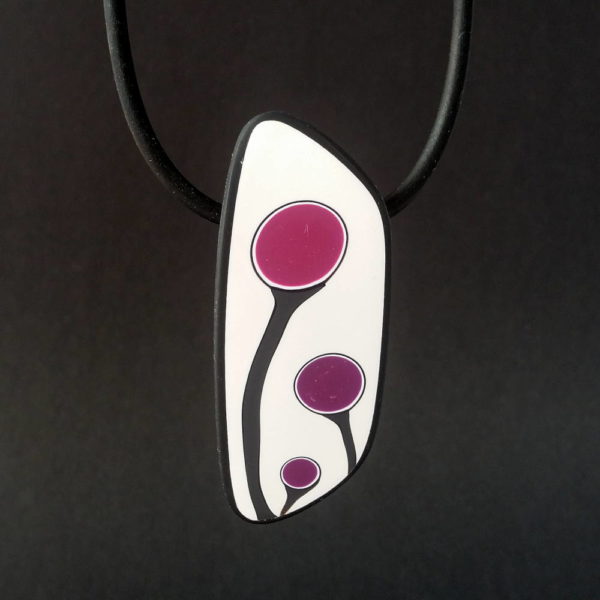 Handmade shield shaped necklace featuring an abstract flower bud motif in plum on a white background, with charcoal border. It is approximately 2.6 cm wide and 6. long and hangs on a black adjustable cord.
