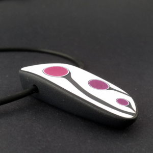 Handmade shield shaped necklace featuring an abstract flower bud motif in plum on a white background, with charcoal border. It is approximately 2.6 cm wide and 6. long and hangs on a black adjustable cord.