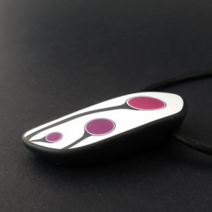 Handmade shield shaped necklace featuring an abstract flower bud motif in plum on a white background, with charcoal border. It is approximately 2.6 cm wide and 6. long and hangs on a black adjustable cord.