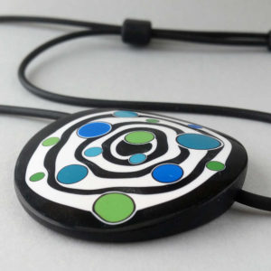 Large handmade pendant with organically-shaped concentric black and white circles, and irregular dots of bright blue and green. It is approximately 6.6cm in diameter and hangs on a black adjustable cord.