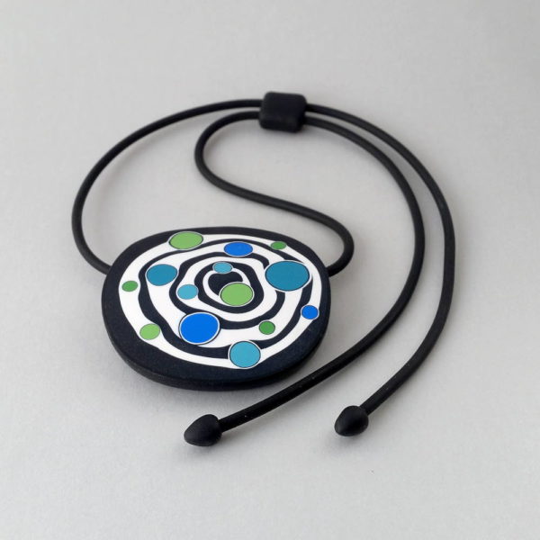 Large handmade pendant with organically-shaped concentric black and white circles, and irregular dots of bright blue and green. It is approximately 6.6cm in diameter and hangs on a black adjustable cord.