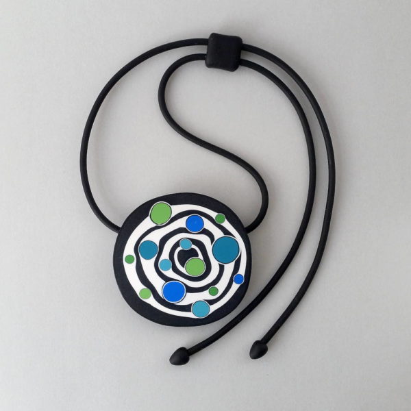 Large handmade pendant with organically-shaped concentric black and white circles, and irregular dots of bright blue and green. It is approximately 6.6cm in diameter and hangs on a black adjustable cord.