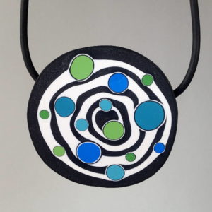 Large handmade pendant with organically-shaped concentric black and white circles, and irregular dots of bright blue and green. It is approximately 6.6cm in diameter and hangs on a black adjustable cord.