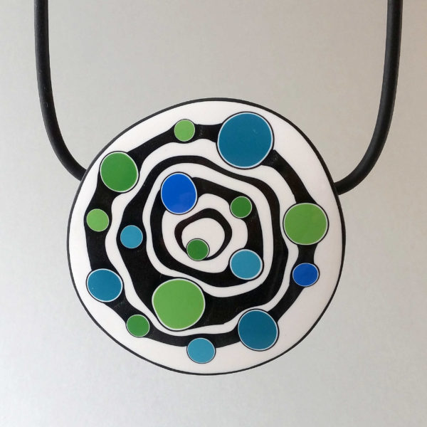 Large handmade pendant with organically-shaped concentric black and white circles, and irregular dots of bright blue and green. It is approximately 6.6cm in diameter and hangs on a black adjustable cord.