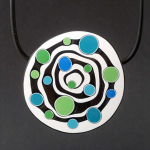 Large handmade pendant with organically-shaped concentric black and white circles, and irregular dots of bright blue and green. It is approximately 6.6cm in diameter and hangs on a black adjustable cord.