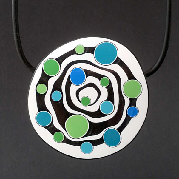 Large handmade pendant with organically-shaped concentric black and white circles, and irregular dots of bright blue and green. It is approximately 6.6cm in diameter and hangs on a black adjustable cord.