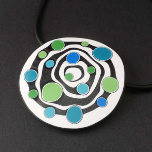 Large handmade pendant with organically-shaped concentric black and white circles, and irregular dots of bright blue and green. It is approximately 6.6cm in diameter and hangs on a black adjustable cord.