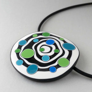 Large handmade pendant with organically-shaped concentric black and white circles, and irregular dots of bright blue and green. It is approximately 6.6cm in diameter and hangs on a black adjustable cord.