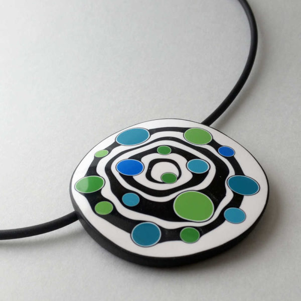 Large handmade pendant with organically-shaped concentric black and white circles, and irregular dots of bright blue and green. It is approximately 6.6cm in diameter and hangs on a black adjustable cord.