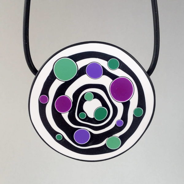 Large handmade pendant with organically shaped concentric black & white circles, and irregular dots of purple, green and magenta. It's approximately 6.6cm in diameter and hangs on a black adjustable cord.