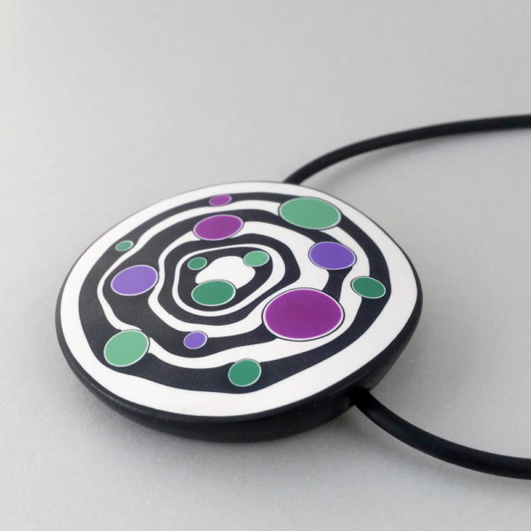 Large handmade pendant with organically shaped concentric black & white circles, and irregular dots of purple, green and magenta. It's approximately 6.6cm in diameter and hangs on a black adjustable cord.