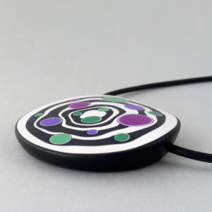 Large handmade pendant with organically shaped concentric black & white circles, and irregular dots of purple, green and magenta. It's approximately 6.6cm in diameter and hangs on a black adjustable cord.