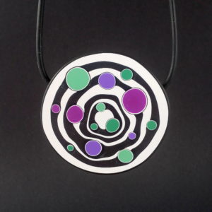 Large handmade pendant with organically shaped concentric black & white circles, and irregular dots of purple, green and magenta. It's approximately 6.6cm in diameter and hangs on a black adjustable cord.