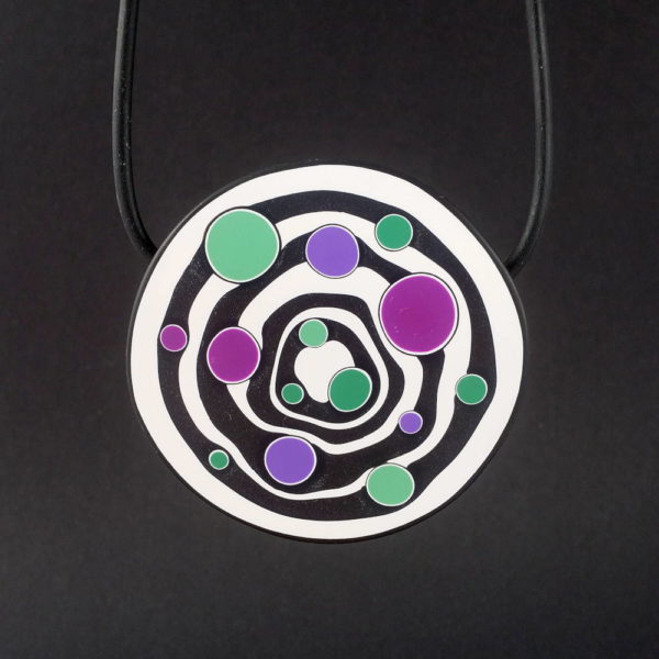 Large handmade pendant with organically shaped concentric black & white circles, and irregular dots of purple, green and magenta. It's approximately 6.6cm in diameter and hangs on a black adjustable cord.