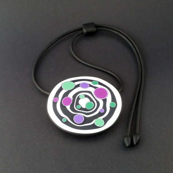 Large handmade pendant with organically shaped concentric black & white circles, and irregular dots of purple, green and magenta. It's approximately 6.6cm in diameter and hangs on a black adjustable cord.