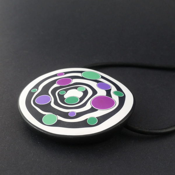 Large handmade pendant with organically shaped concentric black & white circles, and irregular dots of purple, green and magenta. It's approximately 6.6cm in diameter and hangs on a black adjustable cord.