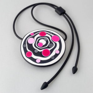 Large handmade pendant with organically-shaped concentric black and white circles, and irregular dots in various pinks. It is approximately 6.6cm in diameter and hangs on a black adjustable cord.