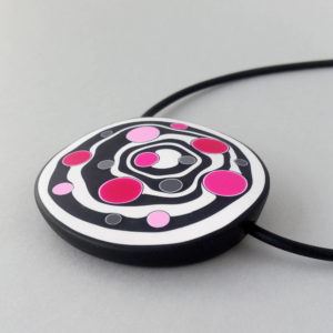 Large handmade pendant with organically-shaped concentric black and white circles, and irregular dots in various pinks. It is approximately 6.6cm in diameter and hangs on a black adjustable cord.