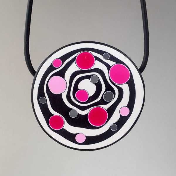 Large handmade pendant with organically-shaped concentric black and white circles, and irregular dots in various pinks. It is approximately 6.6cm in diameter and hangs on a black adjustable cord.