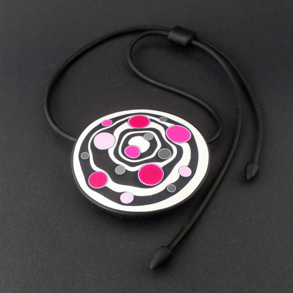 Large handmade pendant with organically-shaped concentric black and white circles, and irregular dots in various pinks. It is approximately 6.6cm in diameter and hangs on a black adjustable cord.