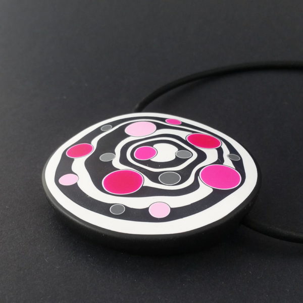 Large handmade pendant with organically-shaped concentric black and white circles, and irregular dots in various pinks. It is approximately 6.6cm in diameter and hangs on a black adjustable cord.