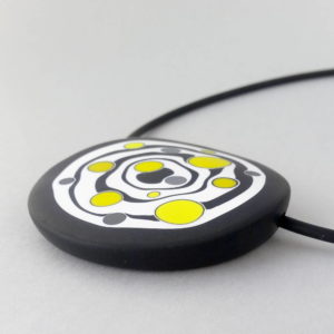 Large handmade pendant with organically-shaped concentric black and white circles, and irregular dots of bright yellow. It is approximately 6.6cm in diameter and hangs on a black adjustable cord.