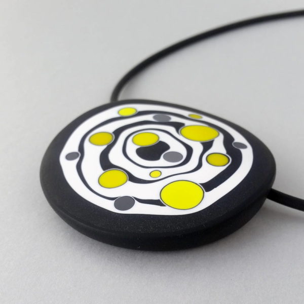 Large handmade pendant with organically-shaped concentric black and white circles, and irregular dots of bright yellow. It is approximately 6.6cm in diameter and hangs on a black adjustable cord.