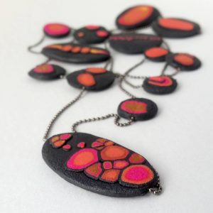 Handmade long necklace with individually crafted flat beads in vibrant orange and magenta on a black, textured background. Length approx. 120cm.