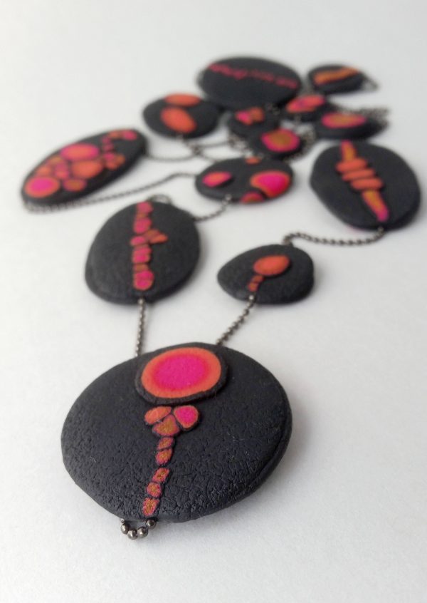 Handmade long necklace with individually crafted flat beads in vibrant orange and magenta on a black, textured background. Length approx. 120cm.