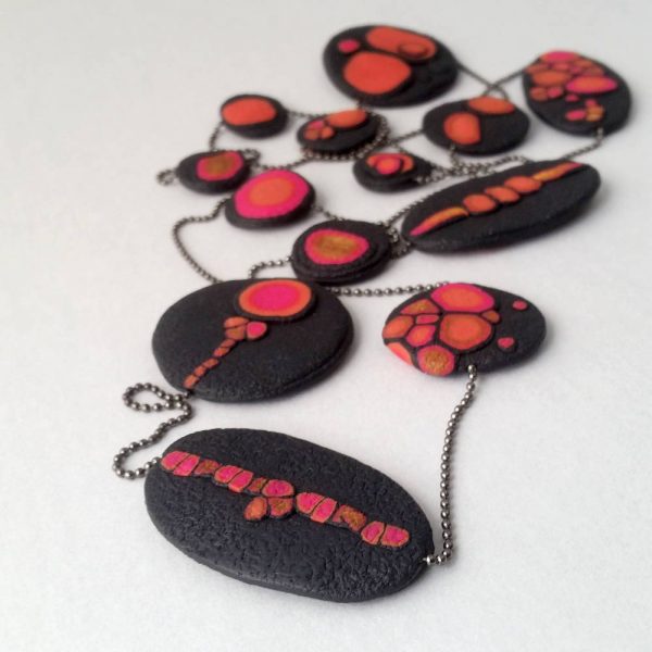 Handmade long necklace with individually crafted flat beads in vibrant orange and magenta on a black, textured background. Length approx. 120cm.