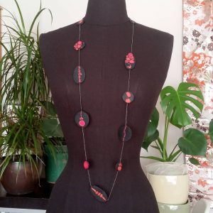 Handmade long necklace with individually crafted flat beads in vibrant orange and magenta on a black, textured background. Length approx. 120cm.