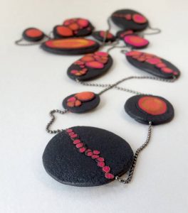 Handmade long necklace with individually crafted flat beads in vibrant orange and magenta on a black, textured background. Length approx. 120cm.