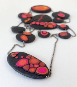 Handmade long necklace with individually crafted flat beads in vibrant orange and magenta on a black, textured background. Length approx. 120cm.