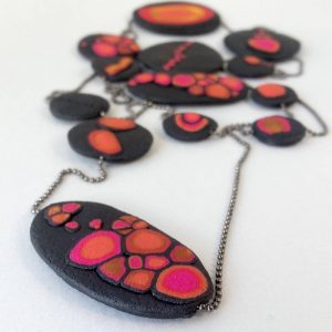 Handmade long necklace with individually crafted flat beads in vibrant orange and magenta on a black, textured background. Length approx. 120cm.