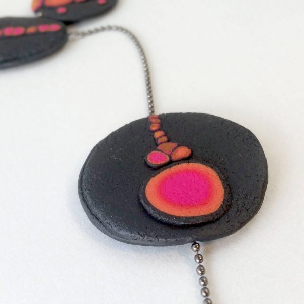 Handmade long necklace with individually crafted flat beads in vibrant orange and magenta on a black, textured background. Length approx. 120cm.