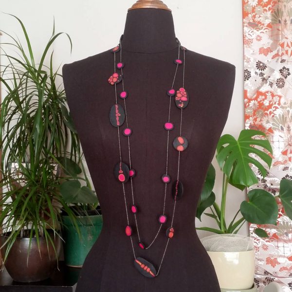 Handmade long necklace with individually crafted flat beads in vibrant orange and magenta on a black, textured background. Length approx. 120cm.