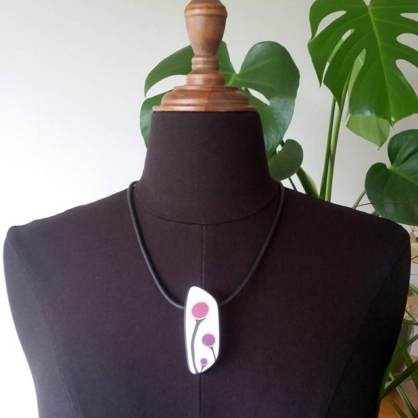 Handmade shield shaped necklace featuring an abstract flower bud motif in plum on a white background, with charcoal border. It is approximately 2.6 cm wide and 6.4cm long and hangs on a black adjustable cord.