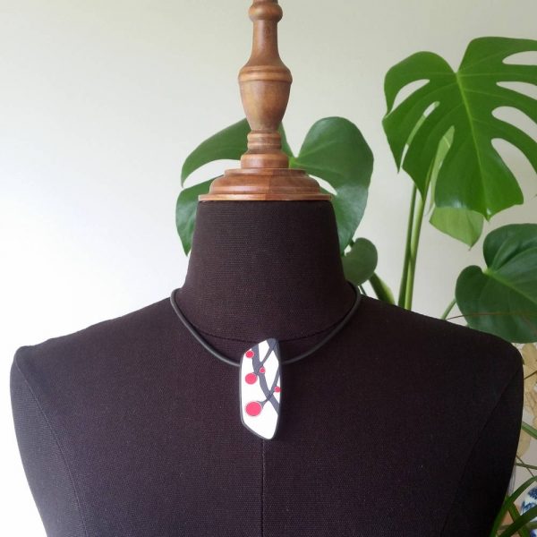 Handmade necklace with a single bead showing a graphic flower bud motif in red, on a white background with a charcoal border. It is approximately 2.6 cm wide and 6.4 cm long and hangs on a black adjustable cord.