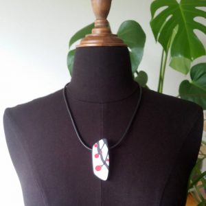 Handmade necklace with a single bead showing a graphic flower bud motif in red, on a white background with a charcoal border. It is approximately 2.6 cm wide and 6.4 cm long and hangs on a black adjustable cord.