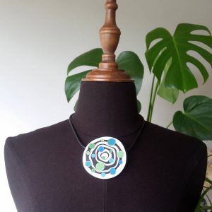 Large handmade pendant with organically-shaped concentric black and white circles, and irregular dots of bright blue and green. It is approximately 6.6cm in diameter and hangs on a black adjustable cord.