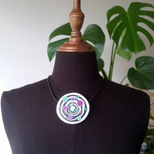 Large handmade pendant with organically shaped concentric black & white circles, and irregular dots of purple, green and magenta. It's approximately 6.6cm in diameter and hangs on a black adjustable cord.